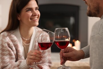 Happy couple with glasses of wine near fireplace at home, selective focus