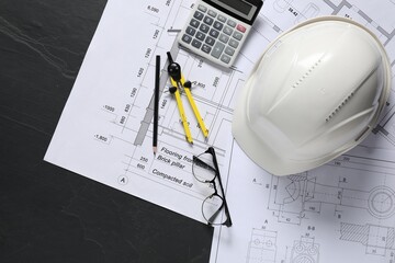 Different engineering drawings, hard hat, pencil, divider, glasses and calculator on black table,...