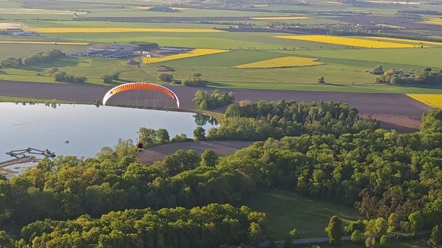 PARAGLIDING aerial panorama of motor-powered paragliding pilot flying above land with engine unit and colorful wing in scenic sky view over meadows and lakes in the countryside	
