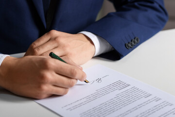 Man putting signature on document at white table, closeup