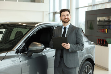 Happy salesman with clipboard near new car in salon