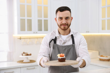 Confectioner with delicious dessert in kitchen, space for text
