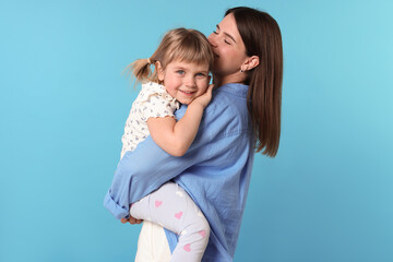 Happy mother and her cute daughter on light blue background