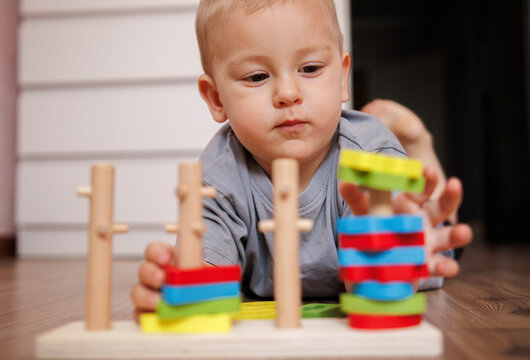 Little boy playing with an educational wooden toy at home. Toddler sorting colorful geometric shapes on pegs. Concept of early childhood development, learning through play, and fine motor skills.