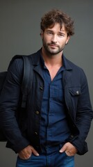 Fototapeta premium Attractive man with backpack studio portrait wearing denim jeans and jacket with hands in pockets confident gaze handsome and casual
