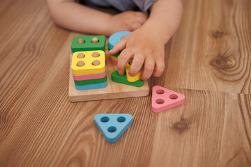 Close-up of child's hands playing with wooden educational toy-sorter. Horizontal photo. Concept of...