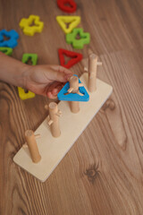 Child’s hand placing shape into wooden Montessori sorting toy. Colorful educational toy for...