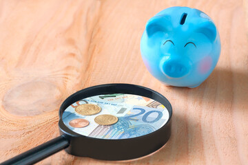 blue piggy bank on wooden floor with magnifying glass.
