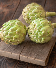 Fototapeta premium Fresh raw artichokes on vintage cutting board with rustic wooden background texture
