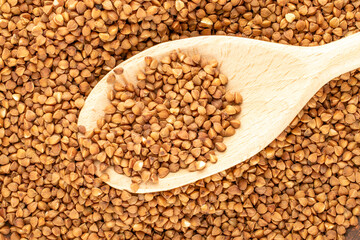 Raw buckwheat with a wooden spoon, top view, macro.