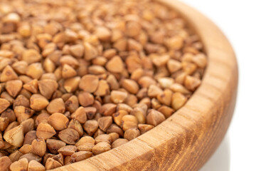Raw buckwheat in a wooden plate isolated on a white background, macro.