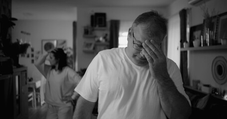 Portrait of man with intense expression during argument, woman in background in living room, focus...