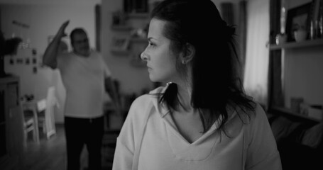 Woman turning her face away in black and white during heated argument, man in background gesturing...
