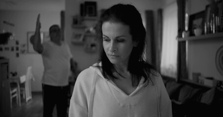 Woman turning her face away in black and white during heated argument, man in background gesturing...