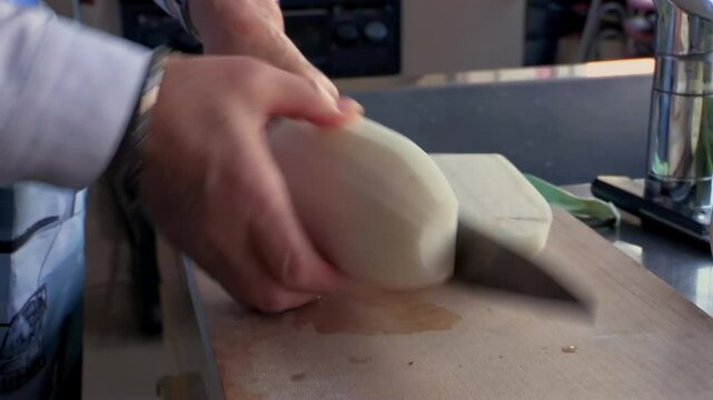 Hands slicing fresh daikon radish on wooden cutting board, home kitchen preparation, root vegetable cooking, traditional meal prep, knife cutting technique, food process