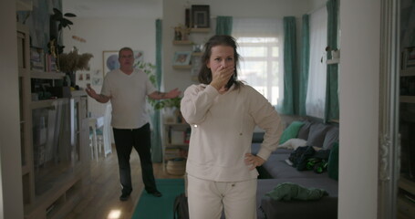 Woman standing resolutely in living room during heated argument with man in background, gesturing...