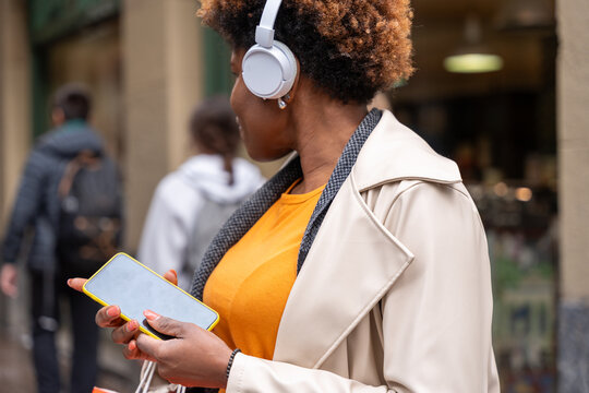 Young woman using smartphone and wearing headphones while walking in the city