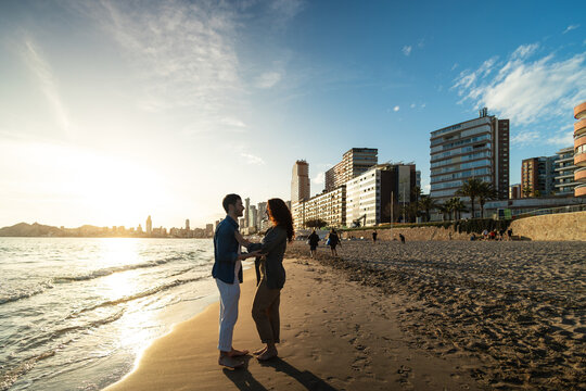 Romantic couple standing barefoot on beach at sunset. Lifestyle. Vacations.