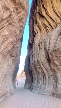 Vertical footage capturing an upward view of the clear blue sky framed by a narrow gap between towering rock formations in AlUla, Hegra, Saudi Arabia, on a sunny day