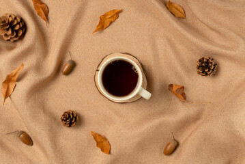 Mug of tea on brown fabric with leaves as concept background. Flat lay, top view.