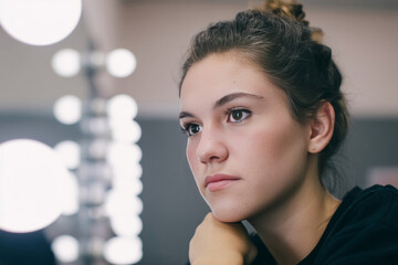Pensive Caucasian woman gazes dreamily amidst vanity bulbs, evoking contemplative aura of World Philosophy Day and Japanese Hanami