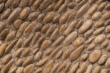Close-up horizontal shot of oval-shaped smooth pebbles arranged in patterns on dry cracked soil, with natural earthy tones and textures.