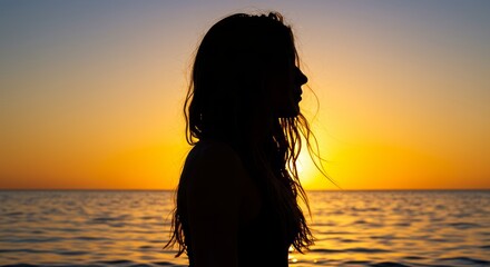 Fototapeta premium Silhouette of a woman gazing at the serene ocean during sunset, evoking a sense of tranquility and peace