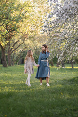 Obraz premium A mother and daughter are walking through a blooming apple orchard. they talk to each other. Concepts of family, mother and child, modern parenting.
