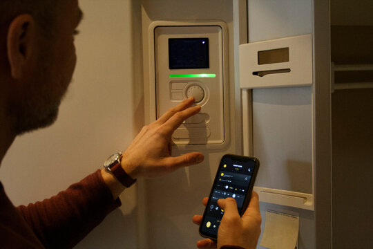 Man adjusting temperature through thermostat while holding smart phone