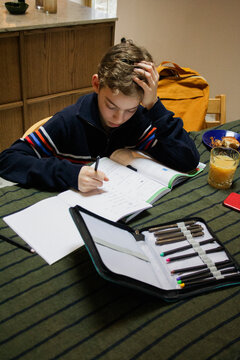 Depressed boy doing homework while sitting at dining table