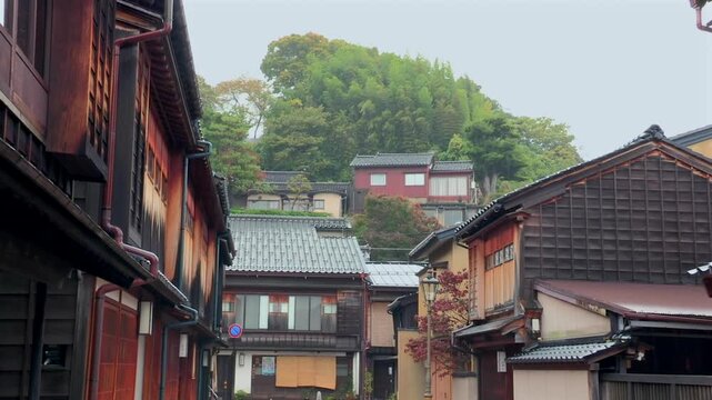 Kanazawa, JAPAN, NOVEMBER 17th, 2010 - Traditional wooden buildings with tiled roofs in historic district, hillside houses surrounded by lush trees and autumn foliage in background