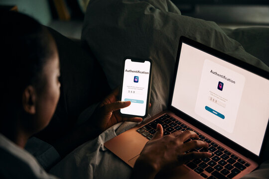 High angle view of woman accessing laptop through smart phone with authentication password while sitting in bedroom at h
