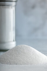 Heap of fine salt and one salt shaker in background on marble countertop.