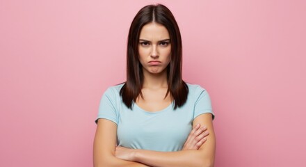 Fototapeta premium Annoyed young woman posing with arms crossed against a pink backdrop