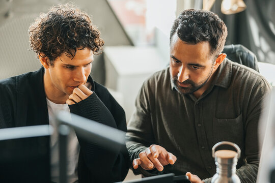 Male computer programmers discussing ideas on smart phone while sitting in office