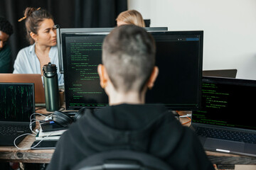 Rear view of non-binary software engineer using computer for coding while analyzing HTML in tech hub