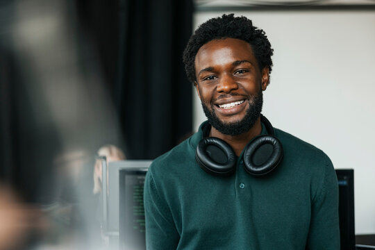 Portrait of male software engineer with wireless headphones around neck in tech startup office