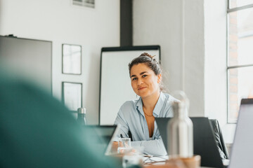 Portrait of smiling young businesswoman sitting at desk in tech startup office