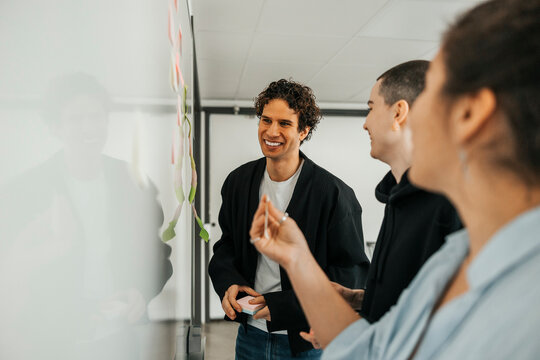 Happy businessman planning strategies with coworkers while standing near whiteboard in office