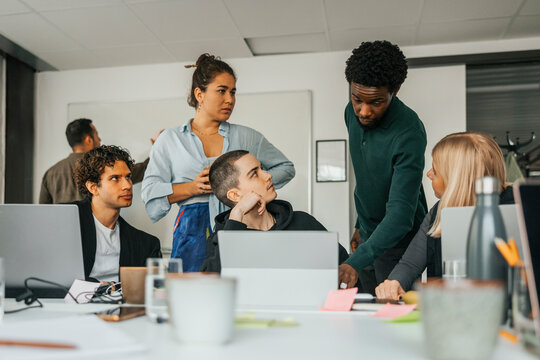 Young businessman sharing ideas while explaining through laptop to coworkers at work place