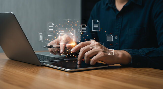 Person using laptop and tablet with digital document icons hovering above on a wooden surface