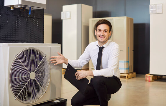 Happy, smiling man shop assistant with clipboard offers modern efficient sustainable ecologically friendly heat pump and HVAC split system for air conditioning available at their home appliances store