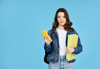 Pretty student girl in denim jacket with backpack and mobile phone looking at camera on blue background.