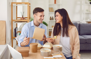 Young man and woman sitting with cardboard boxes eating fresh healthy food delivered from online...