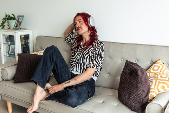 Young non-binary person relaxing on sofa listening to music with headphones