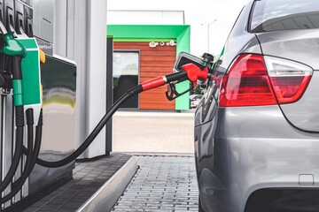 A gun in a car tank at a gas station. Against the background of a column with fuel hoses of binzin,...