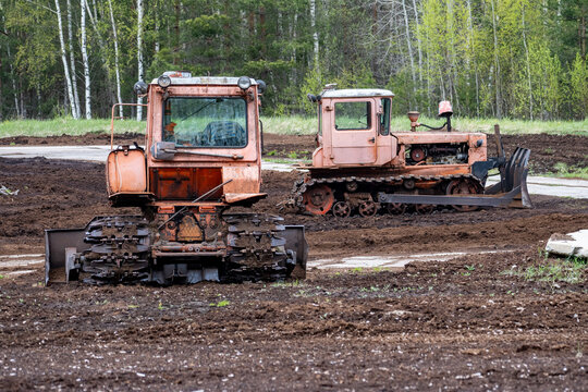 Old Soviet Tracked Bulldozers on Construction Site in Forest Area – Abandoned Rusty Industrial Machinery on Muddy Ground - Powered by Adobe