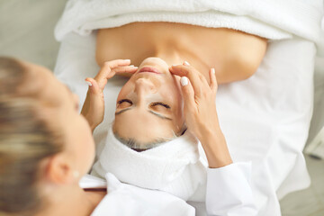 Cosmetologist applies fabric nourishing mask to woman's face for rejuvenation and elimination of...