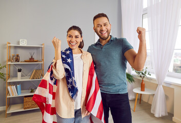 Portrait of a happy family couple wrapped in the American flag at home, celebrating Independence...