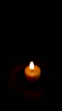 Una toma de cerca de una vela amarilla con llama desenfocada rodeada de varias luces con bombillos de varios colores en movimiento en la oscuridad. Video Vertical
